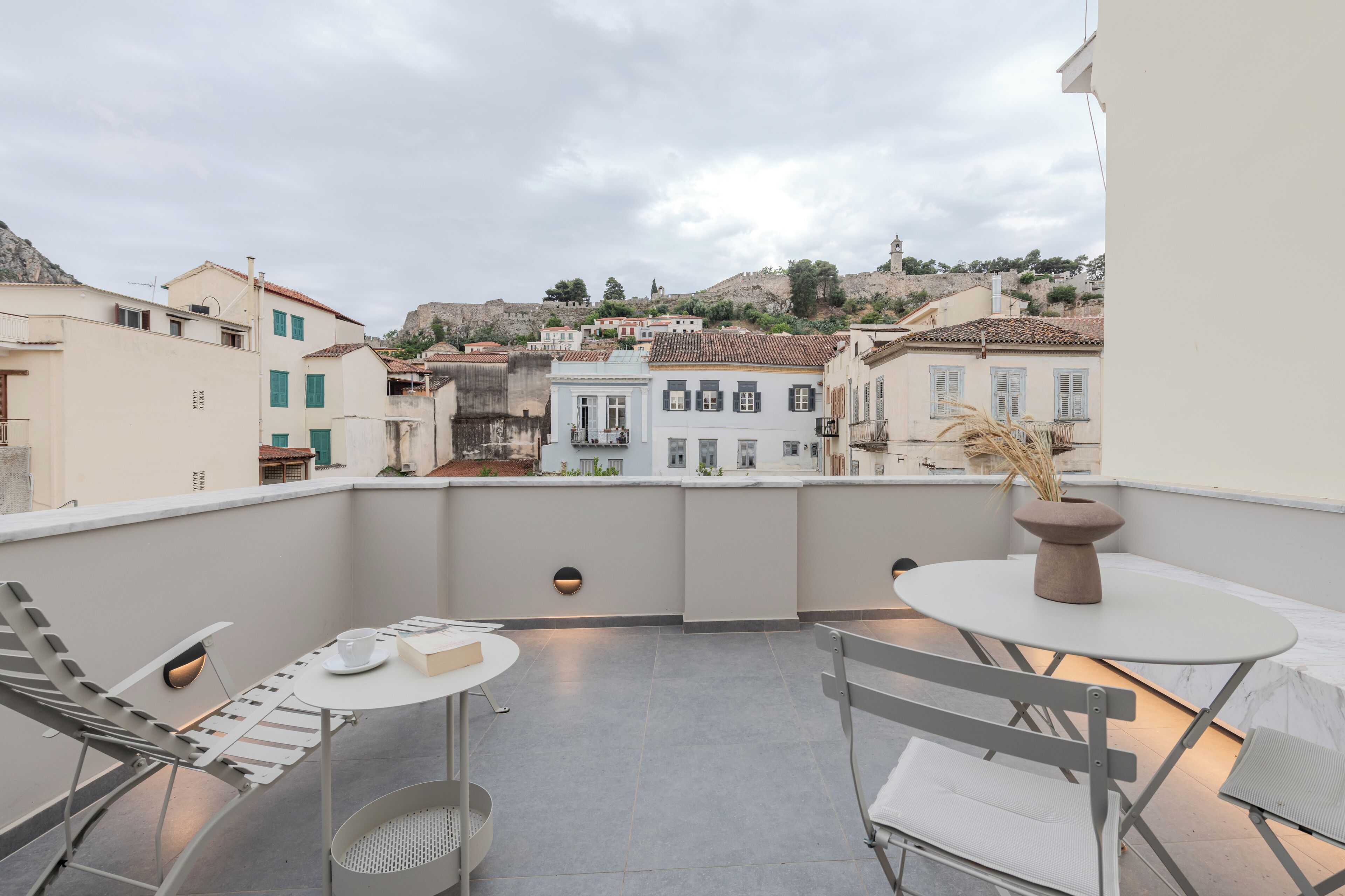 Una terraza en la azotea con una mesa, sillas, una planta en maceta y vistas de la ciudad.