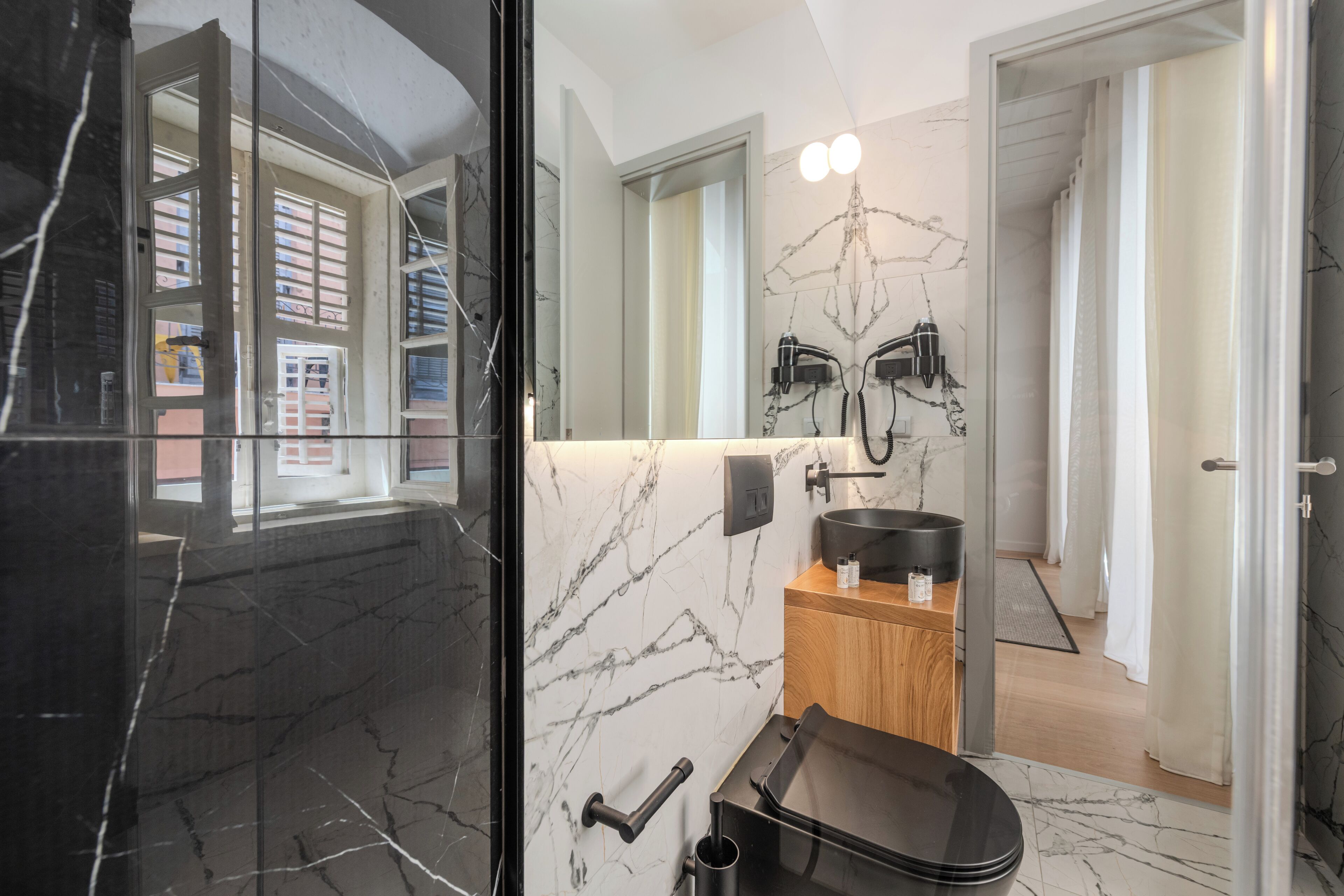 Een moderne badkamer met een marmeren spatwand, een zwart wastafel en een spiegel met een uniek ontwerp.