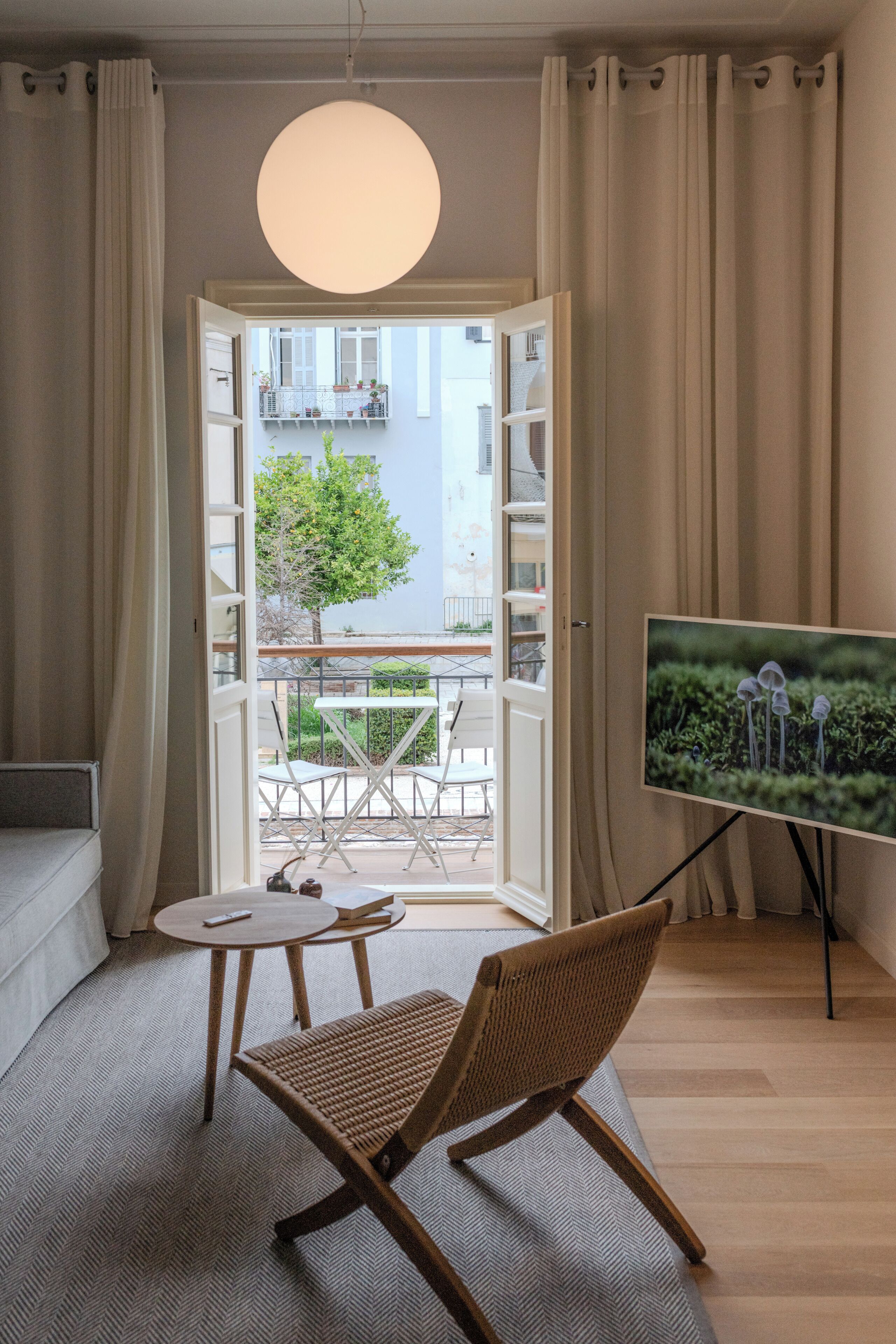 Una sala moderna con un sofá, una mesa redonda, una silla de mimbre, un televisor y vistas a un balcón con mobiliario exterior.