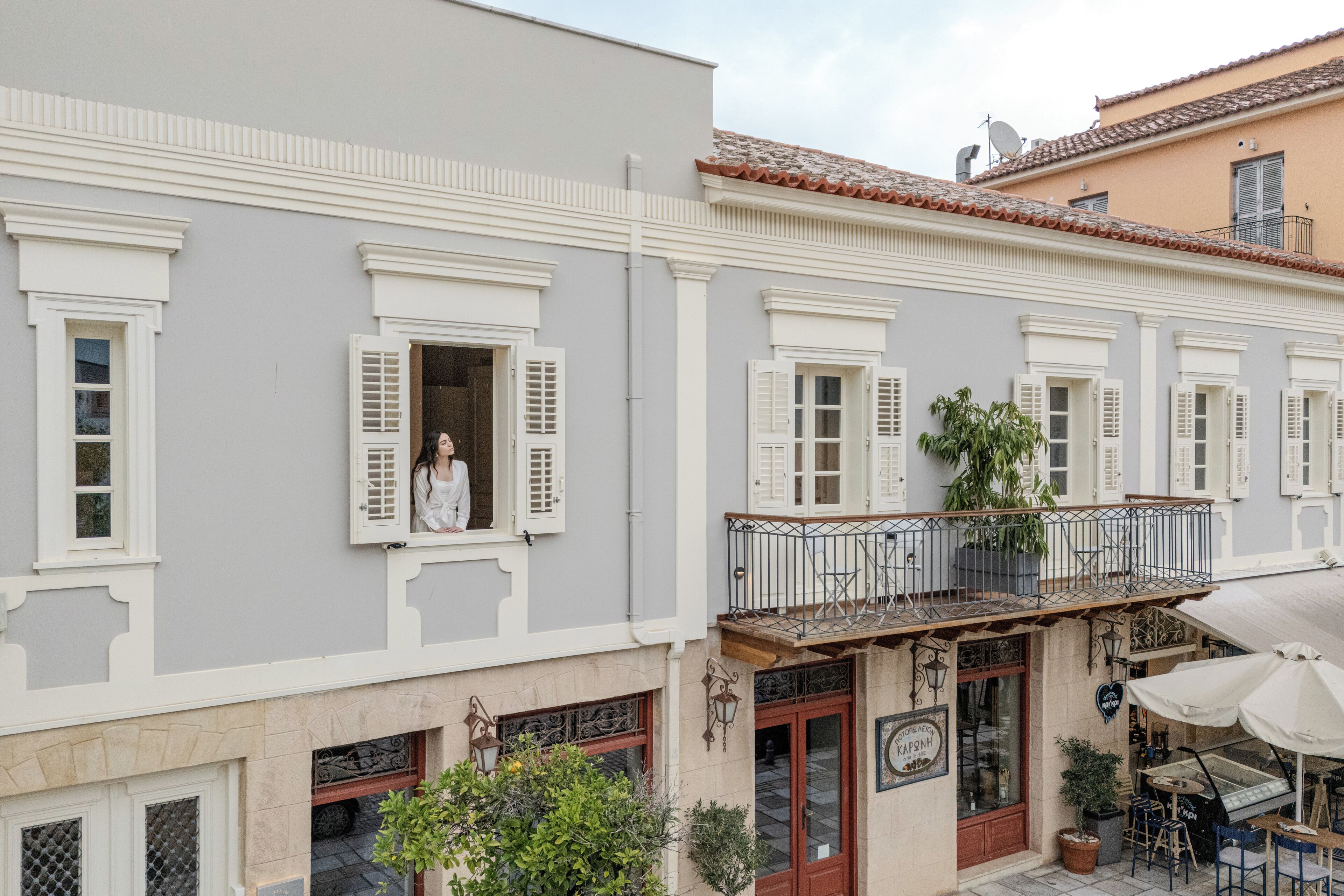 A building with a balcony, a shop with a sign, and outdoor seating.