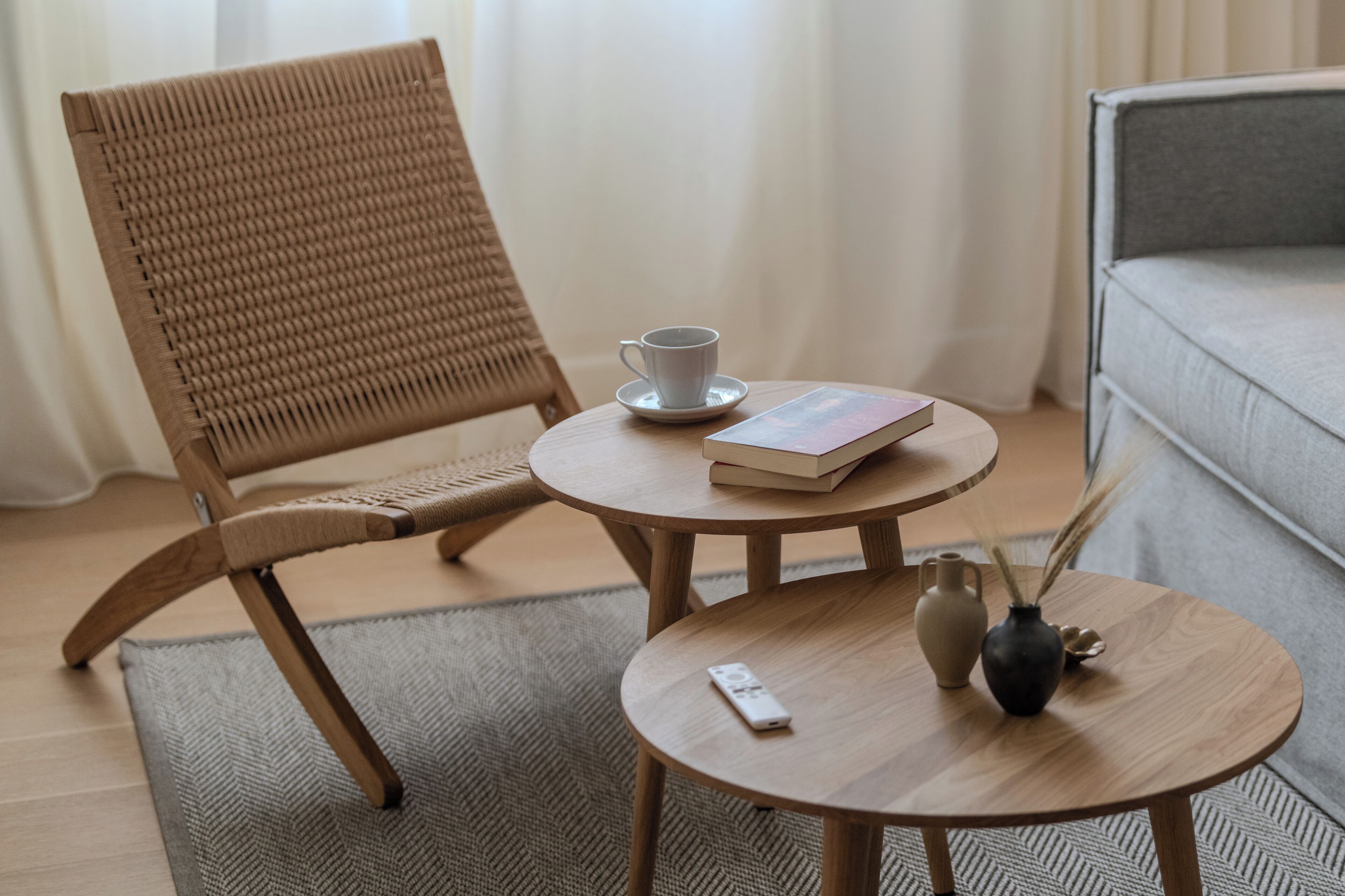 A wooden chair, a small round table with a book, a cup, a vase, and a remote control.