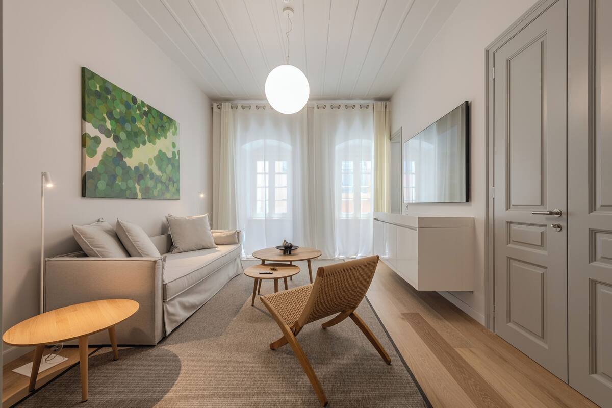 A modern living room with a sofa, a round table, a wicker chair, and a painting on the wall.