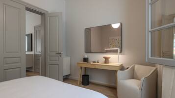 A bedroom with a bed, a desk, a chair, a mirror, and a trash can.