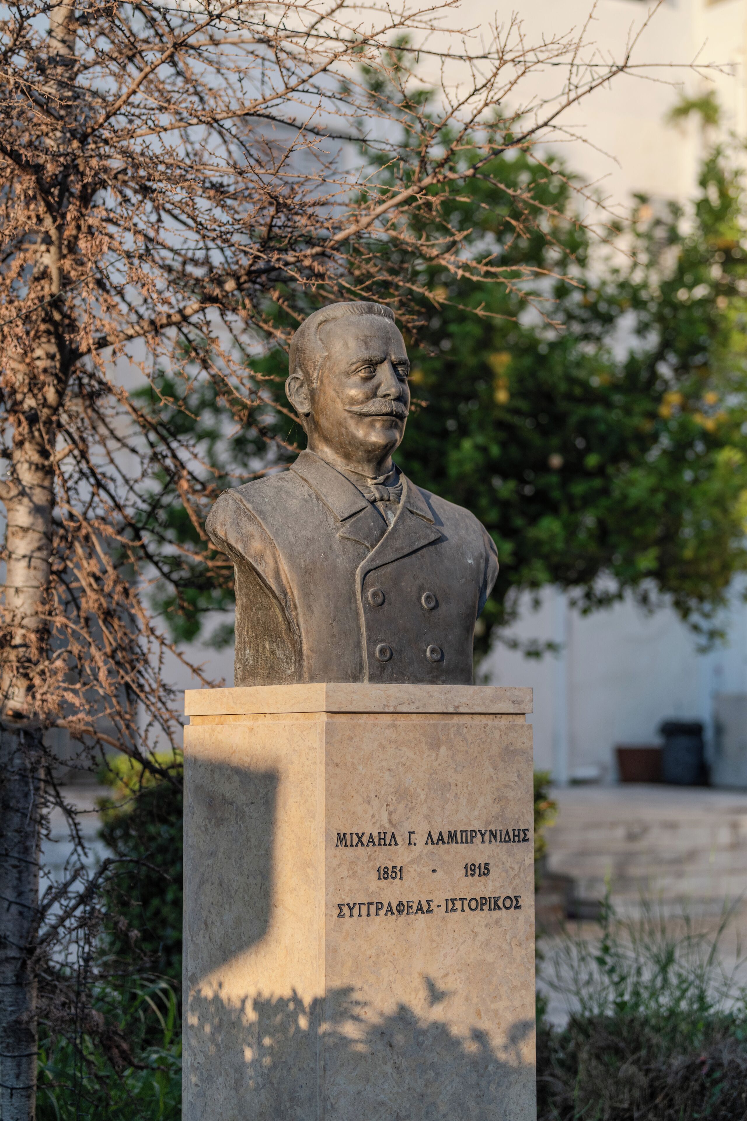 Busto de homem com placa de identificação em frente a uma árvore.