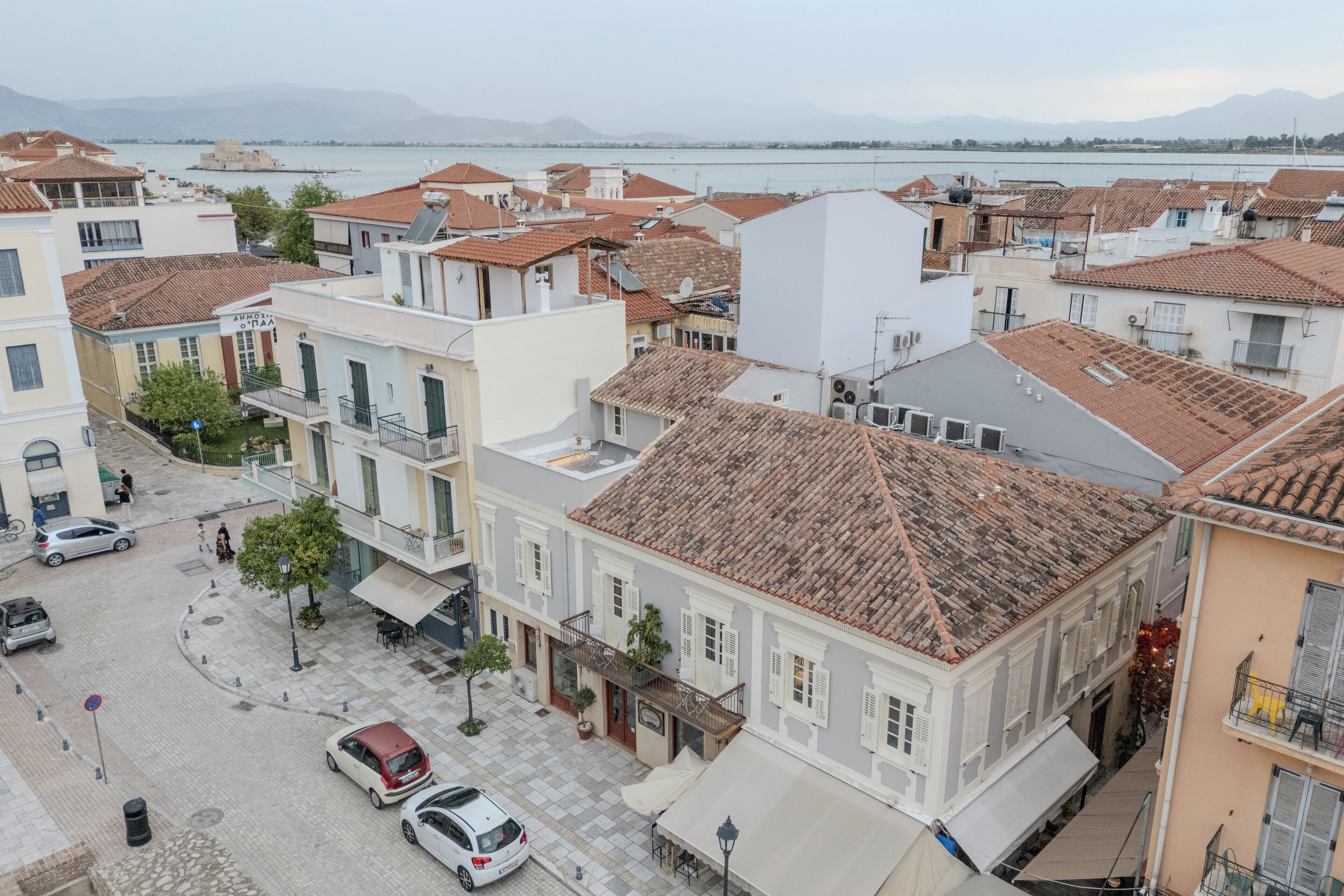 A coastal town with terracotta-roofed buildings, a paved street, and parked cars.