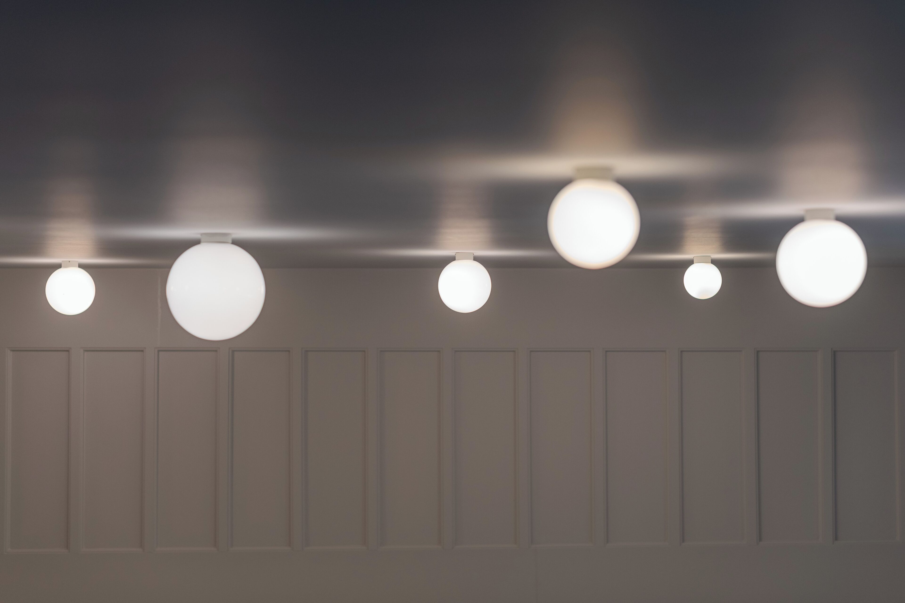 A row of ceiling-mounted spherical light fixtures against a wall with paneling.