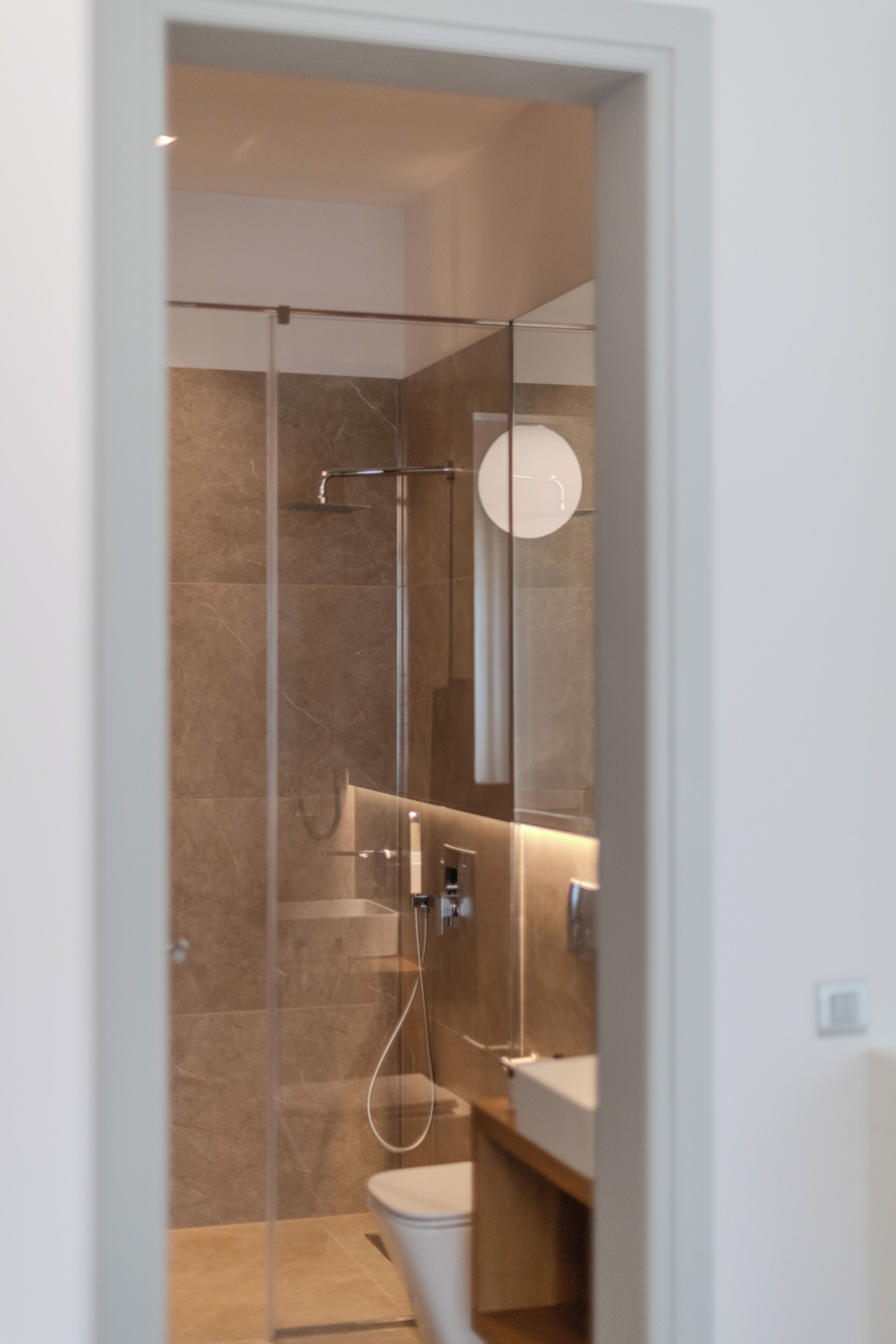 A modern bathroom with a glass shower enclosure, a white toilet, and a wooden vanity.