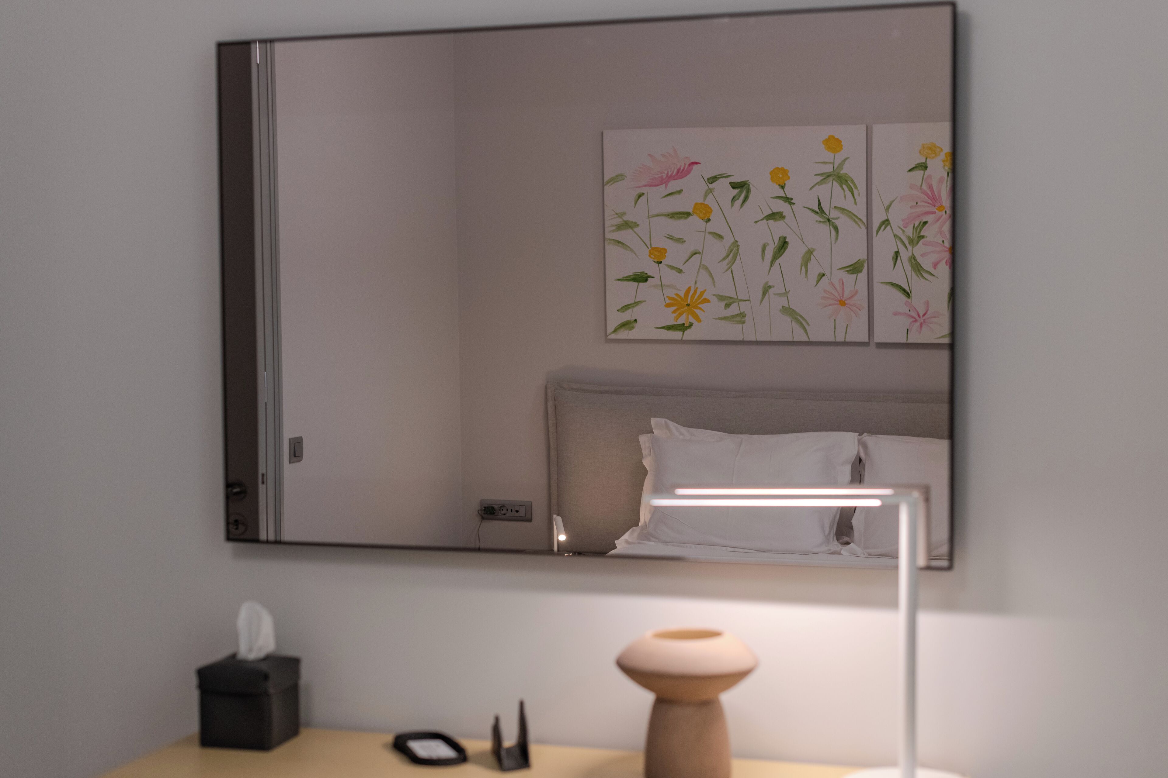 A bedroom with a large mirror, a bedside lamp, a tissue box, and a small table.