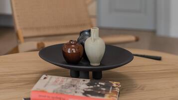 A round wooden table with a black base, a small brown vase, a white vase, and a stack of books.