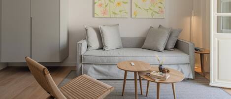 A modern living room with a grey sofa, two round wooden tables, a woven chair, and floral artwork on the wall.