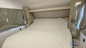A bunk bed with a patterned mattress in a room with wooden walls and a sloped ceiling. - Cozy 2-bedroom RV in Serene Jerusalem with WiFi, AC, and plenty space to sleep (Jerusalem)
