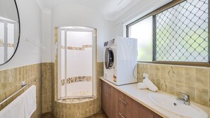 A bathroom with a shower, a washing machine, a sink, and a window with a view.