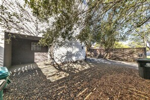 Outdoor space with a garage door, mulch groundcover, and a trash bin.