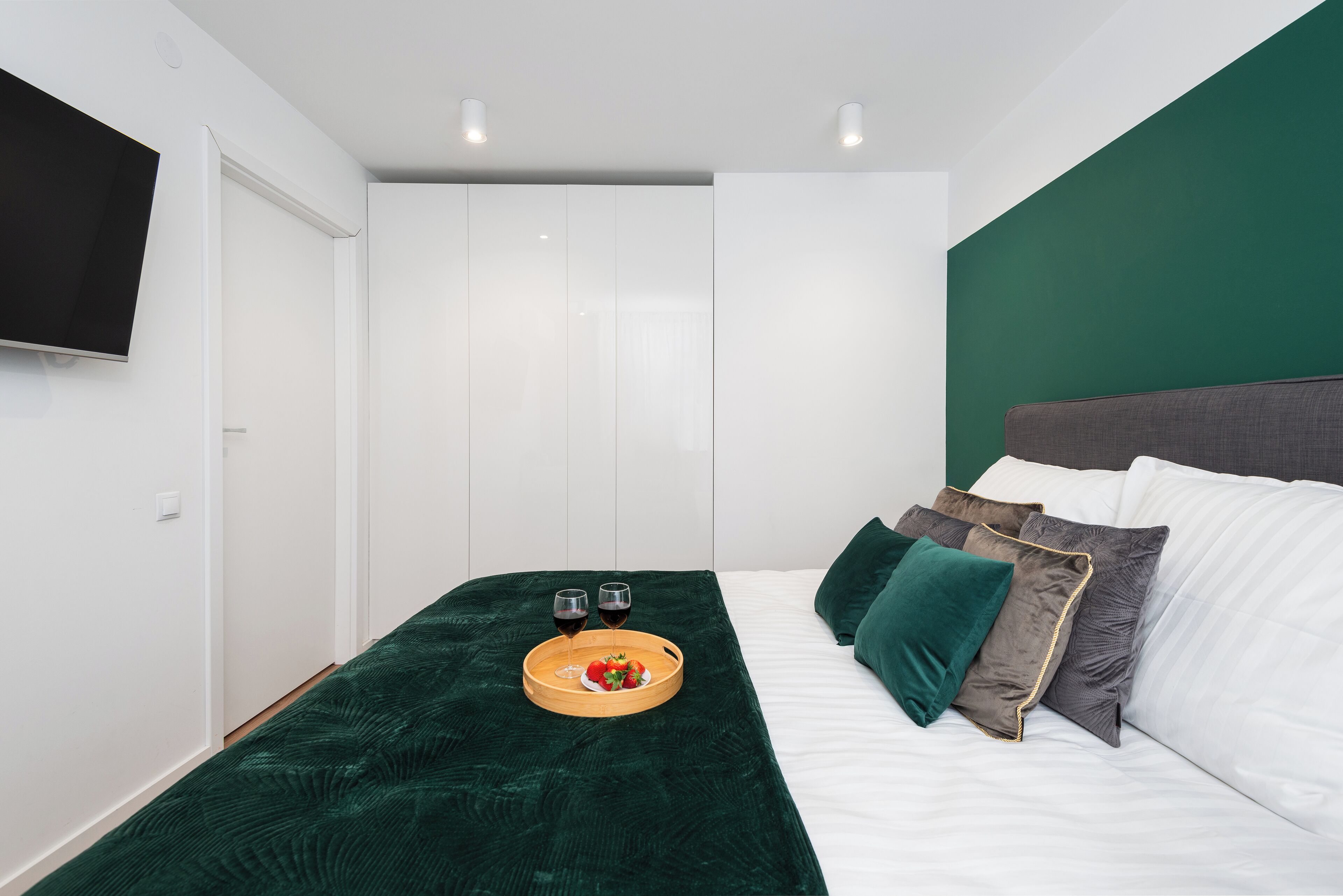 A bedroom with a bed, a green headboard, white bedding, and a tray with glasses and fruit.