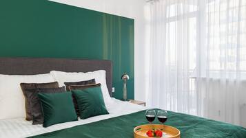 A neatly made bed with green bedding, two glasses of red wine, and a tray with strawberries on a wooden tray.