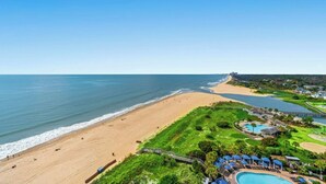 Un complejo turístico frente al mar con playa de arena, piscina y vistas al océano.