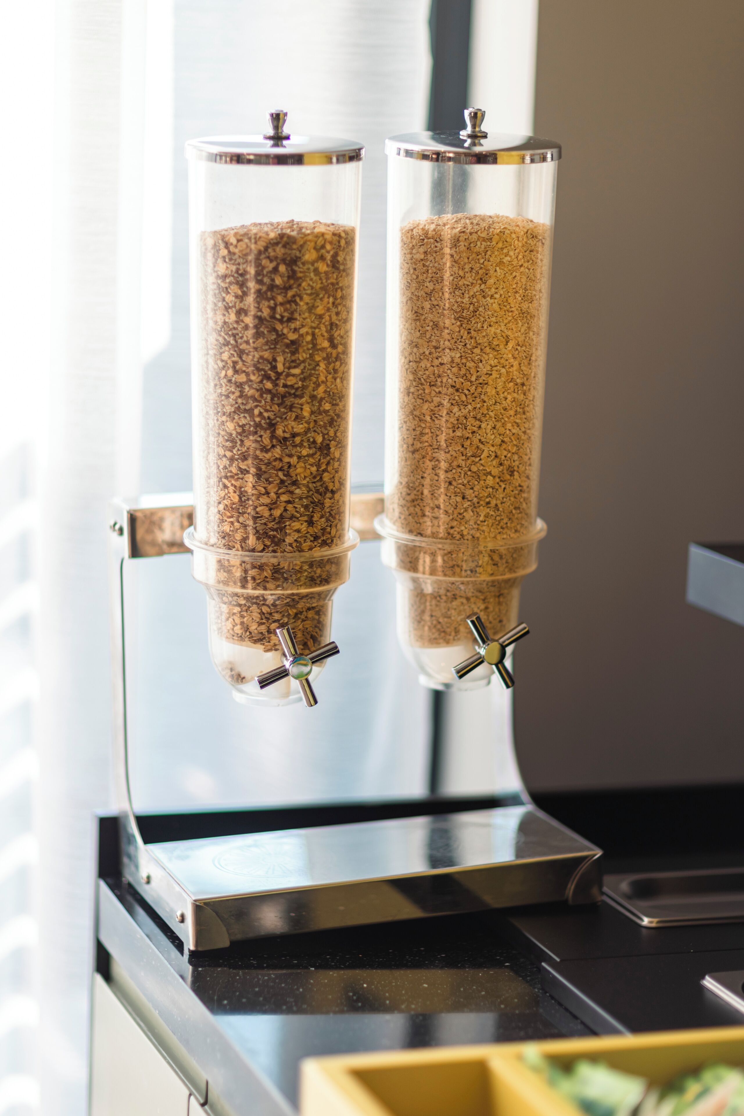 Due distributori cilindrici pieni di granola, montati su un supporto metallico.