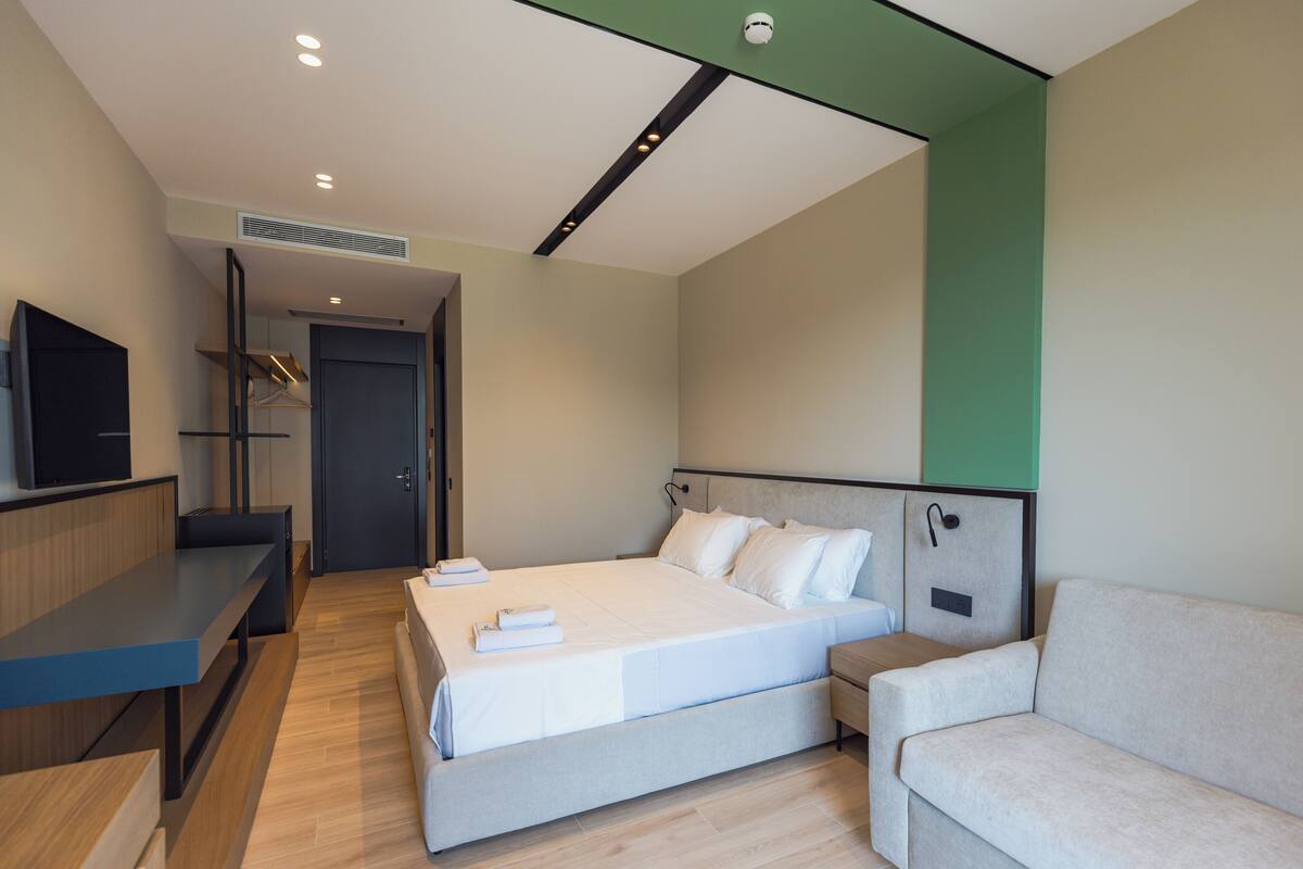 Una habitación de hotel moderna con cama, sofá, escritorio y televisor.