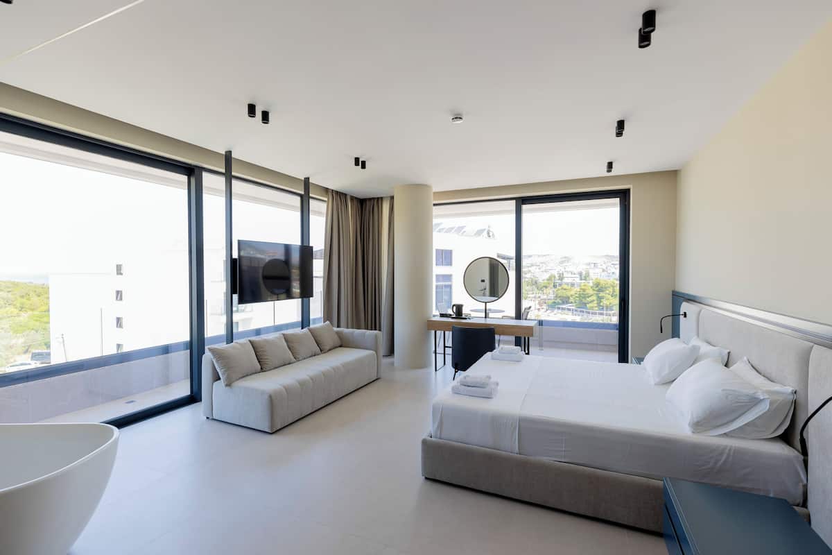 Una habitación de hotel moderna con una cama grande, un sofá, un escritorio con una silla y un ventanal con vistas a la ciudad.