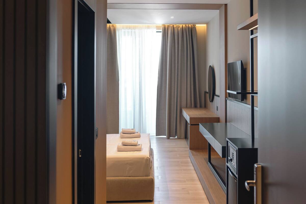 Habitación de hotel moderna con piso de madera, cama, televisión y un minibar.