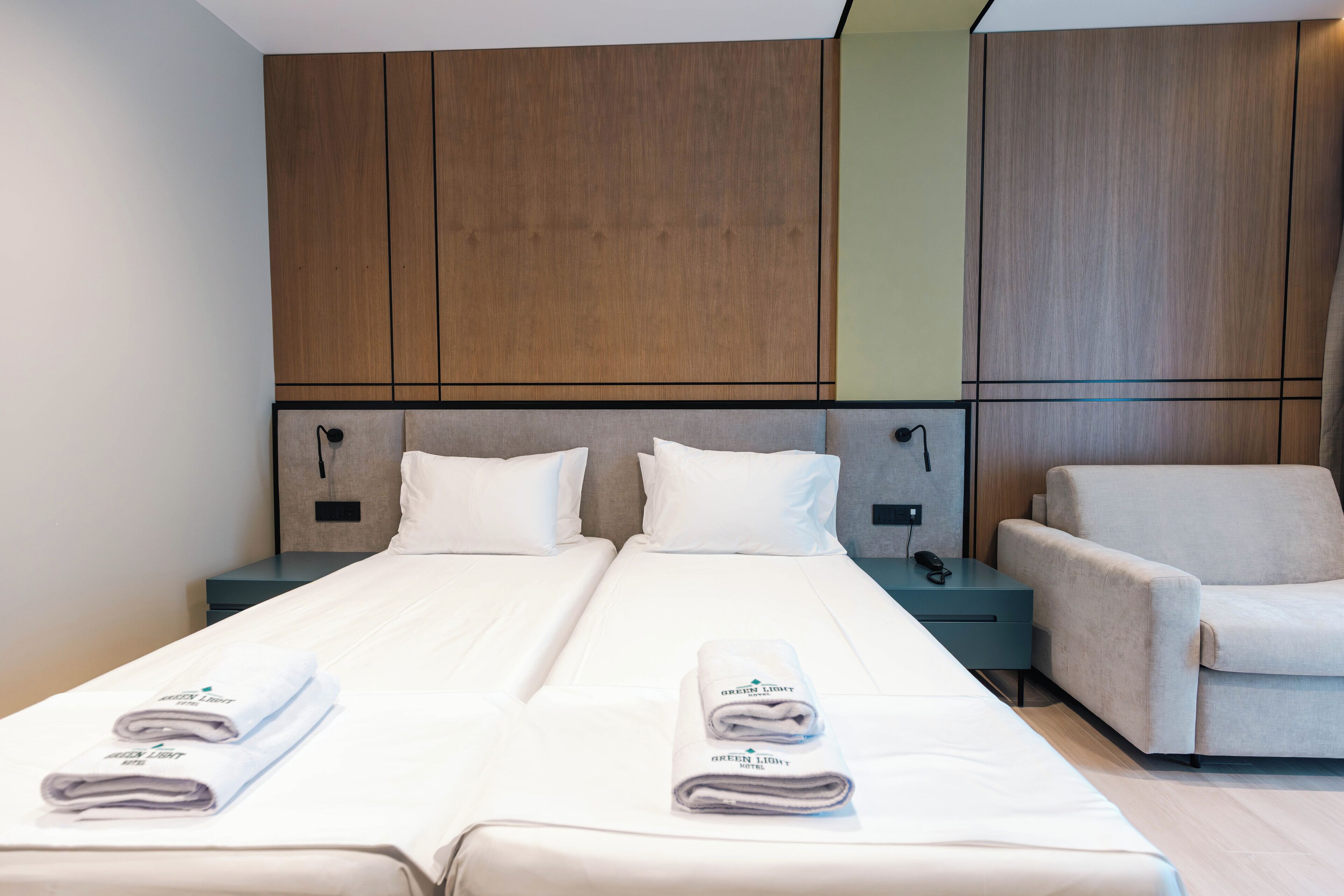 A hotel room with two beds, a sofa, and wooden paneling on the walls.
