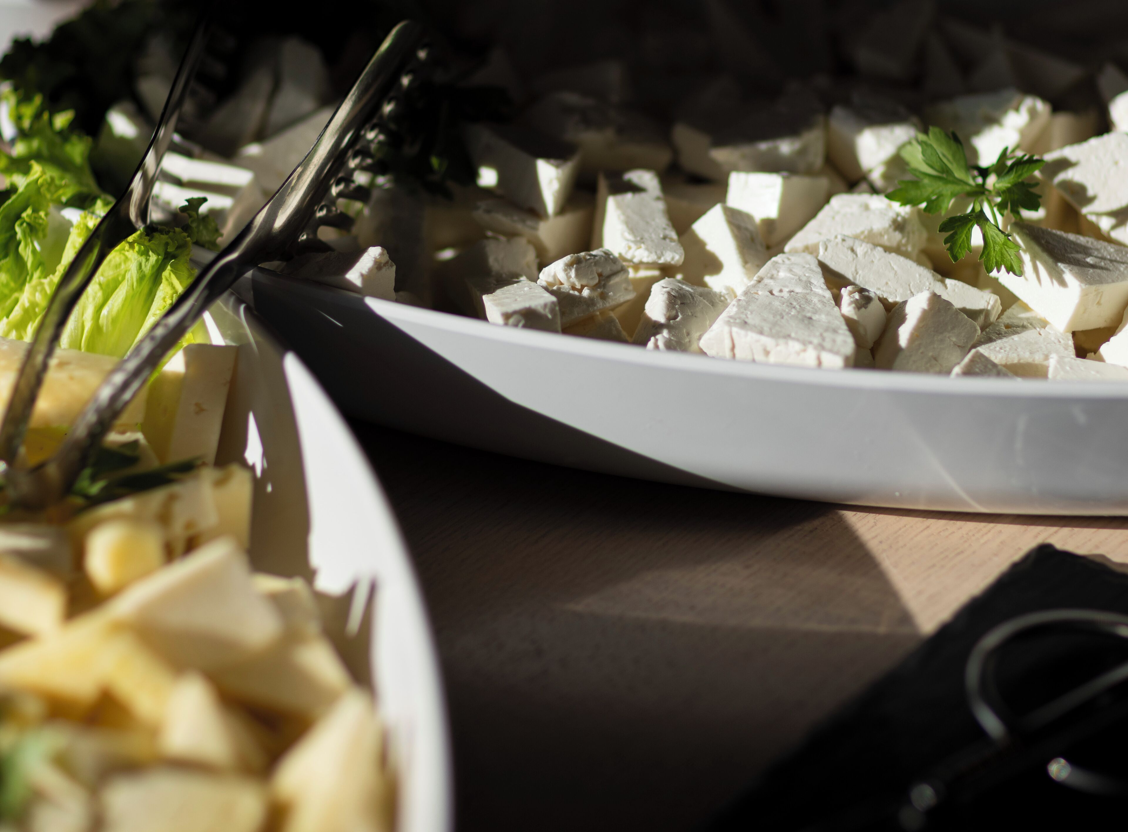 Un plato blanco con queso en cubos y una ramita de perejil sobre una mesa de madera.