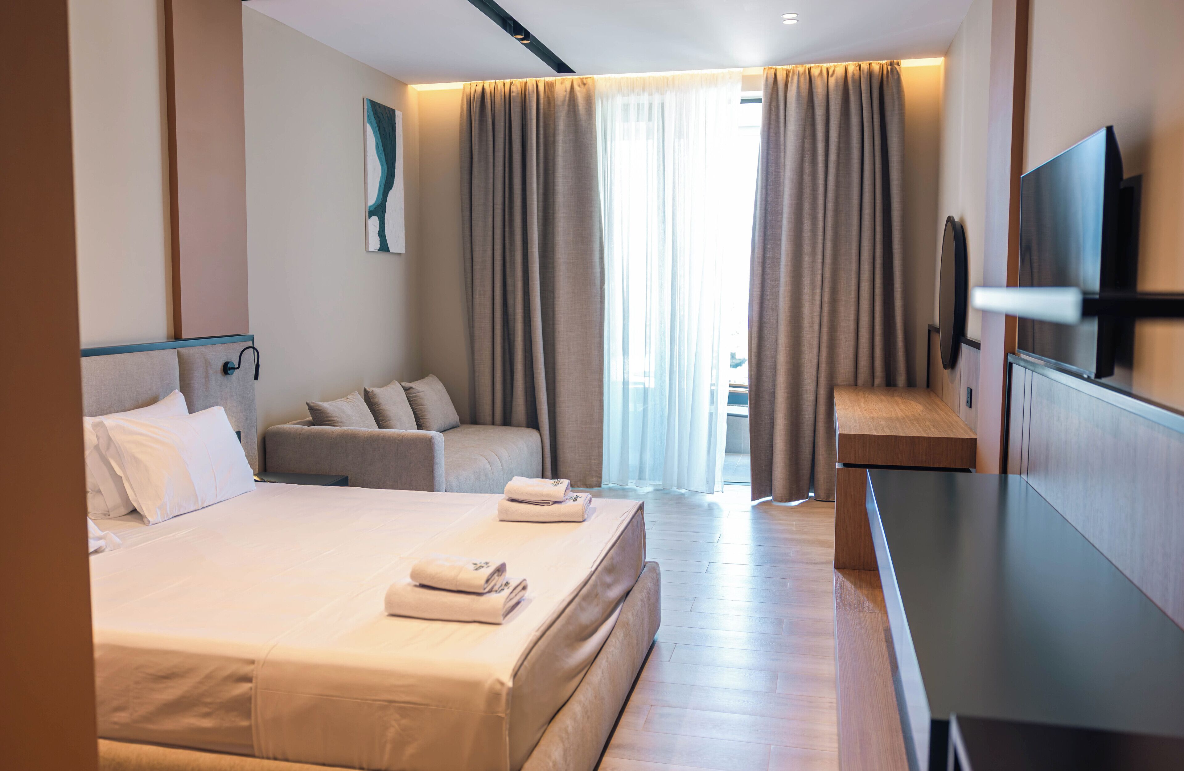 Ein Hotelzimmer mit einem großen Bett, einer Sitzecke, einem Fernseher und Blick ins Freie.