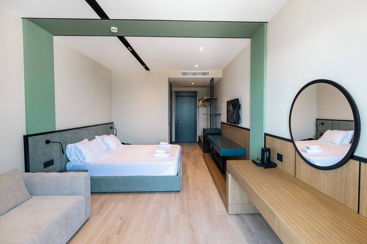 Una habitación de hotel moderna con cama, mesita de noche, espejo, banco y zona de estar.