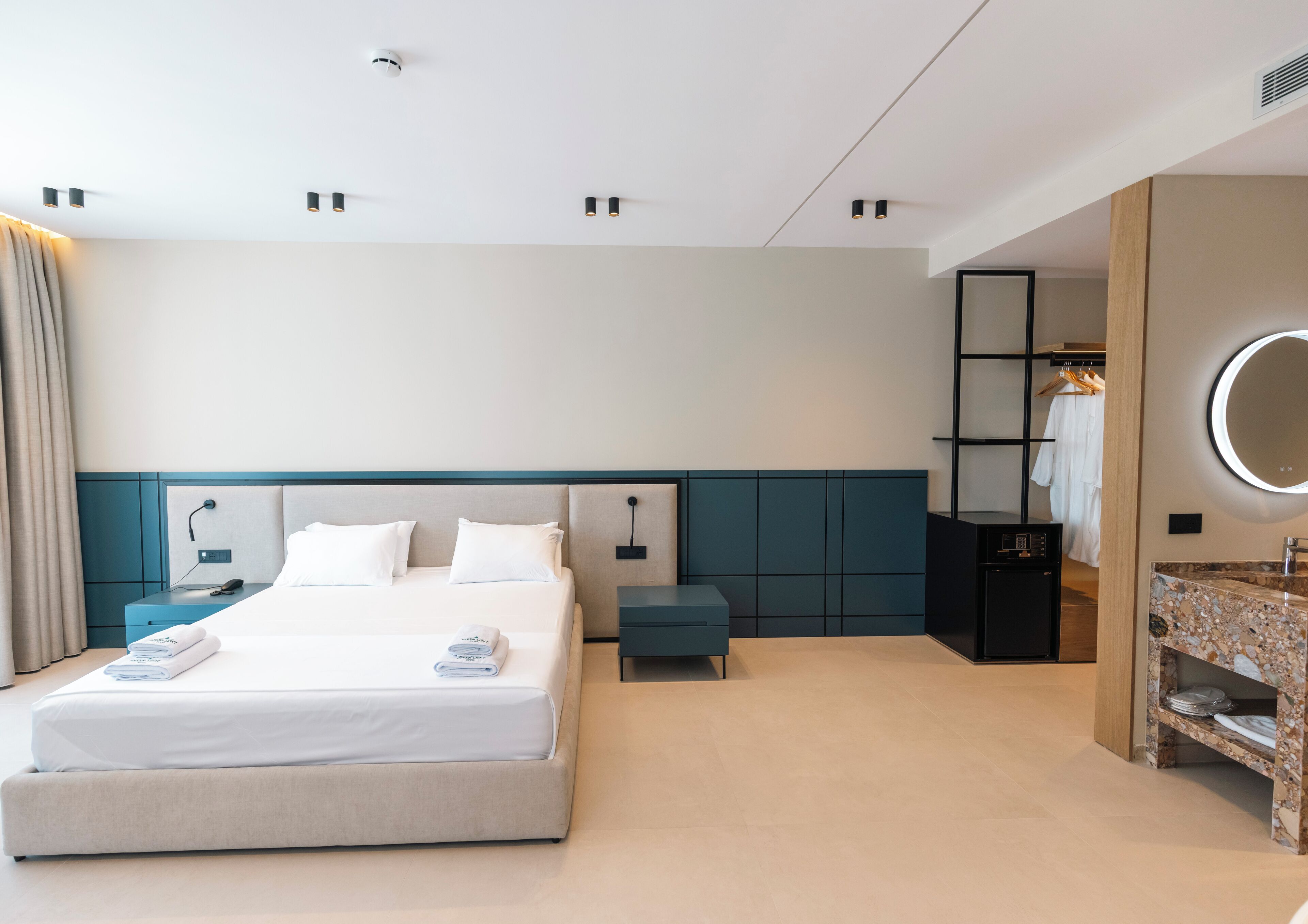 Ein modernes Hotelzimmer mit einem großen Bett, Nachttischen, einem Schminktisch mit Spiegel und einem begehbaren Kleiderschrank.