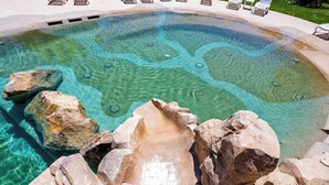 Une piscine aux eaux cristallines, bordée de rochers et de chaises longues.
