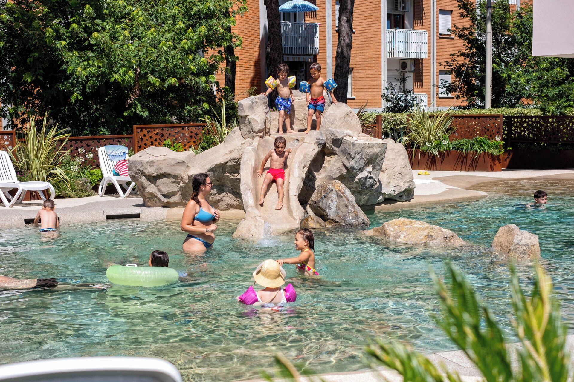 A swimming pool area with clear water, rocks, and lounge chairs.