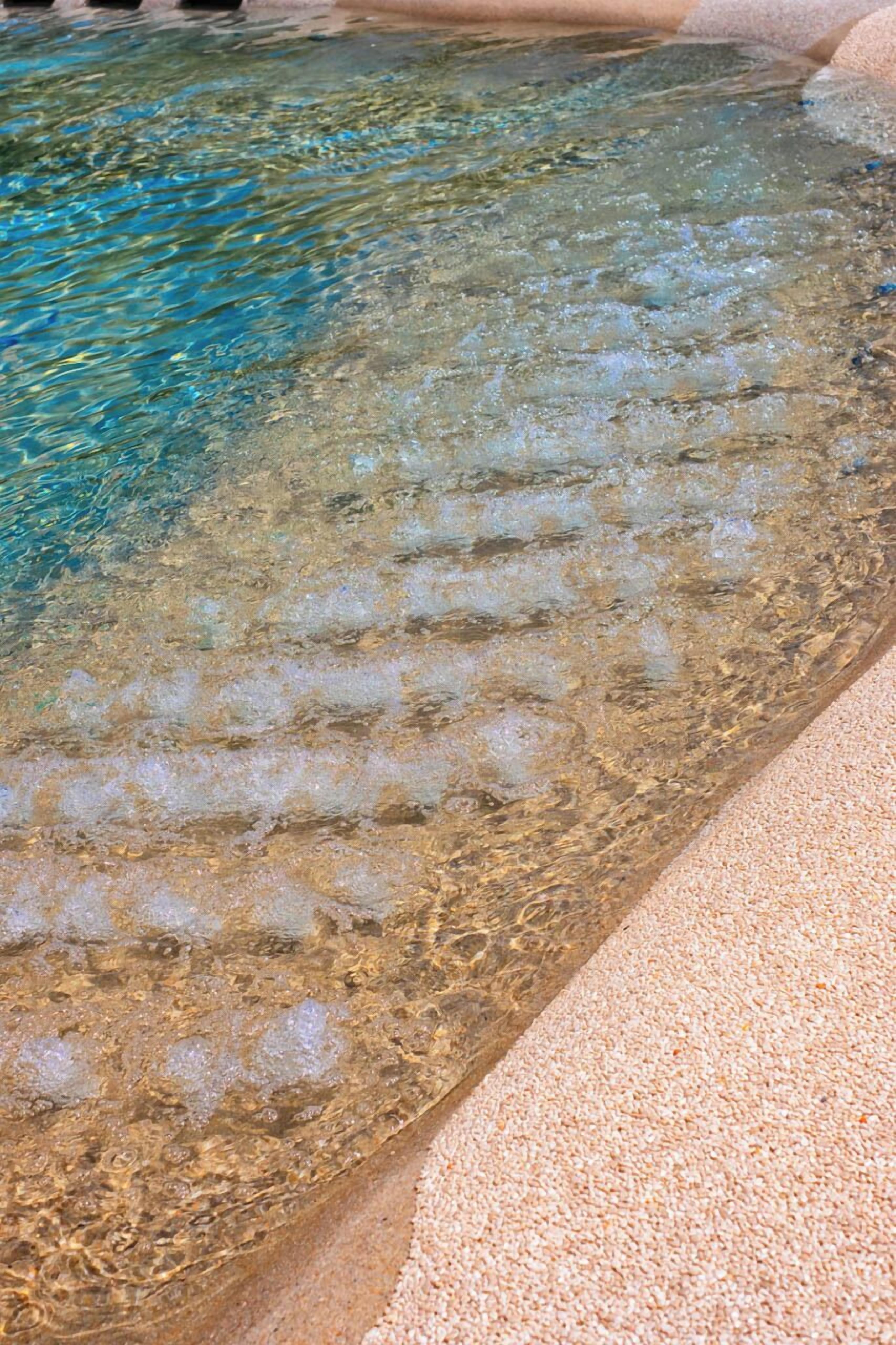 A clear pool with visible water movement and a sandy edge.