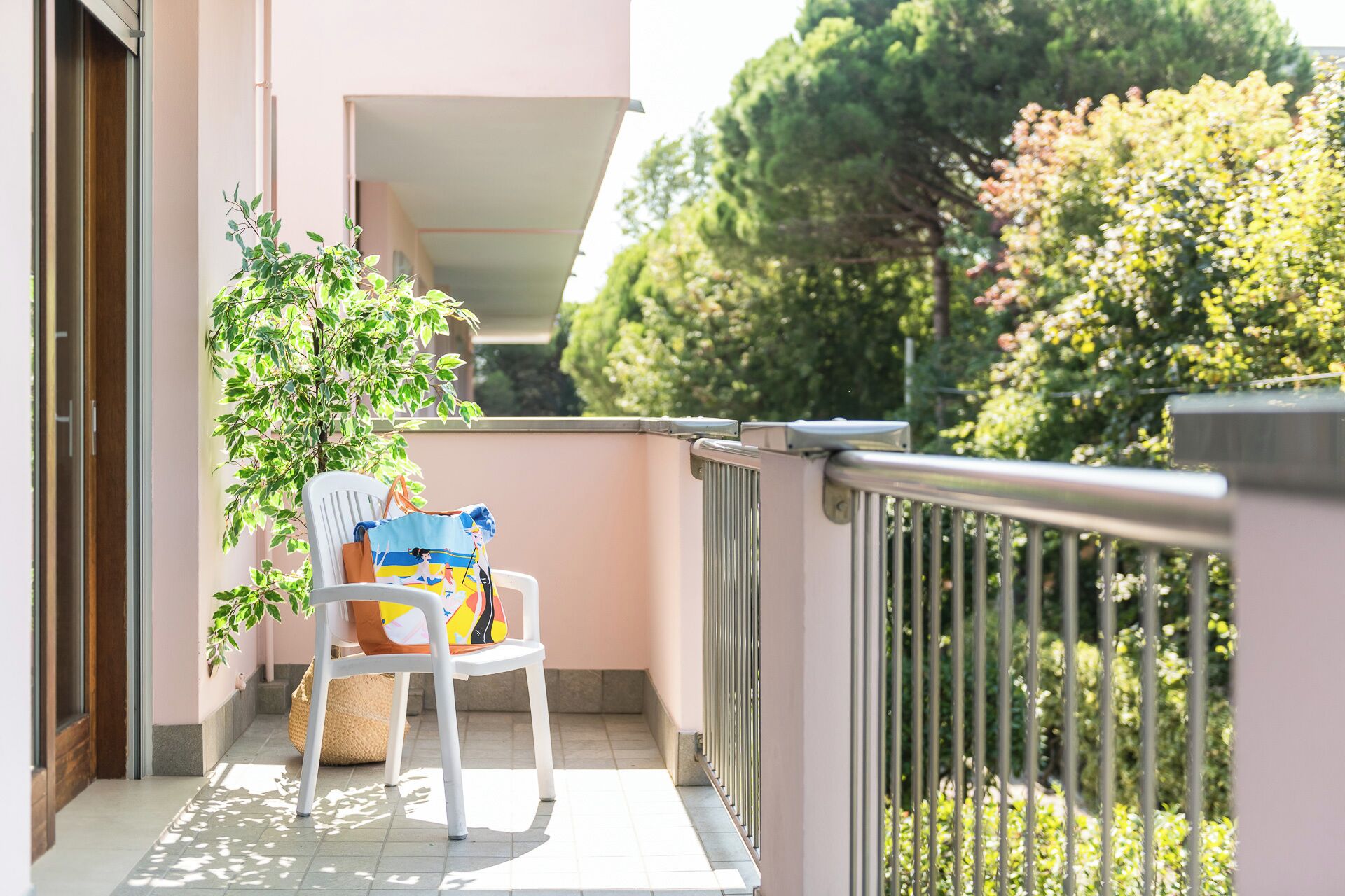 Un balcon avec une chaise blanche, un sac coloré et une plante en pot.
