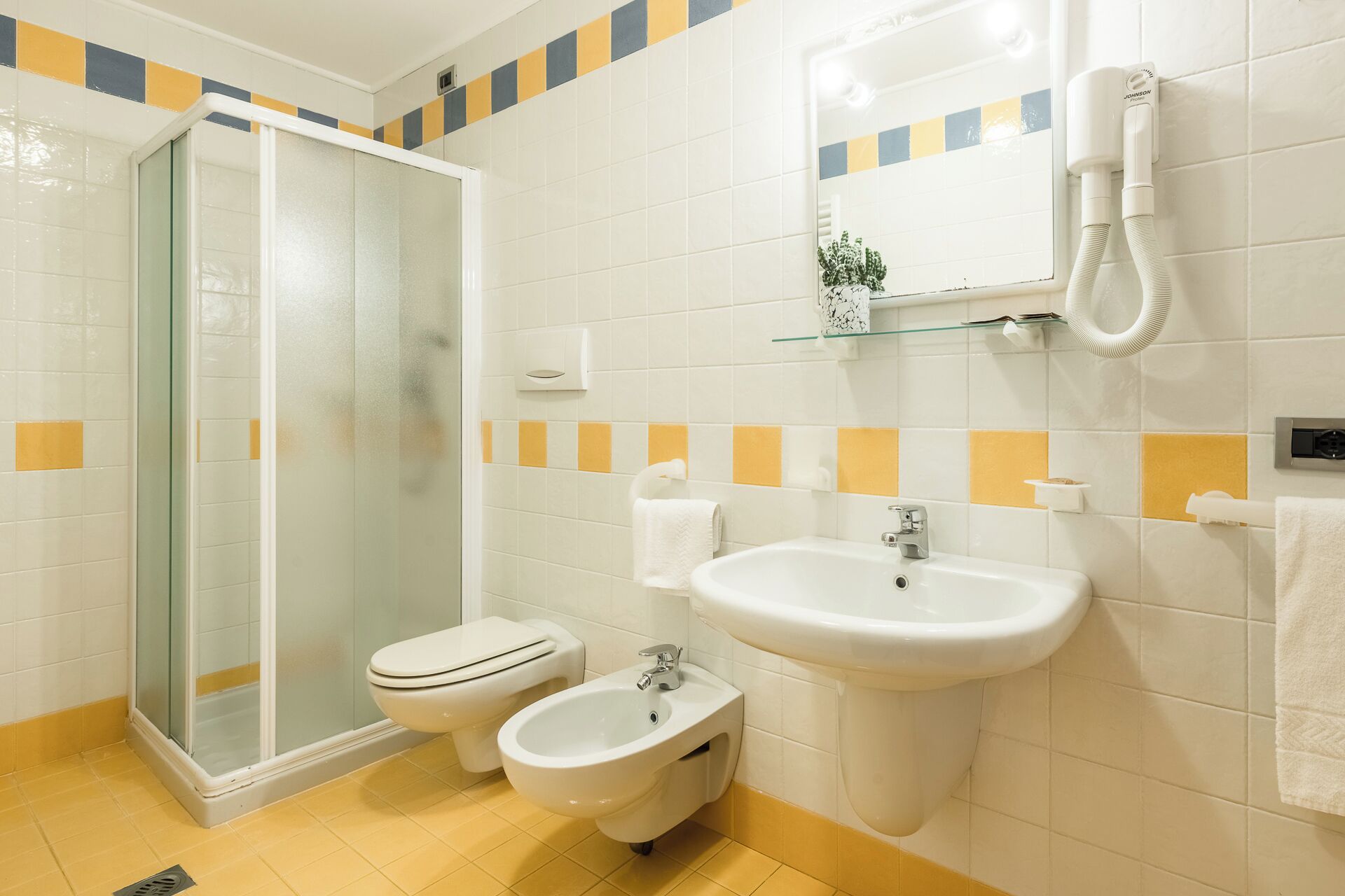 Ein Badezimmer mit Duschkabine, Toilette, Bidet, Waschbecken und Spiegel.