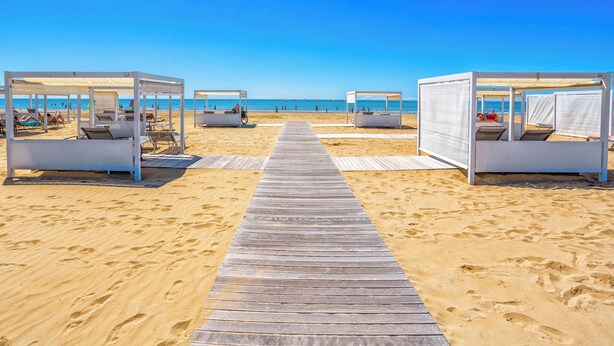 Une plage dotée de passerelles en bois menant à de petits abris de plage blancs, chacun équipé d’un espace pour s’asseoir.