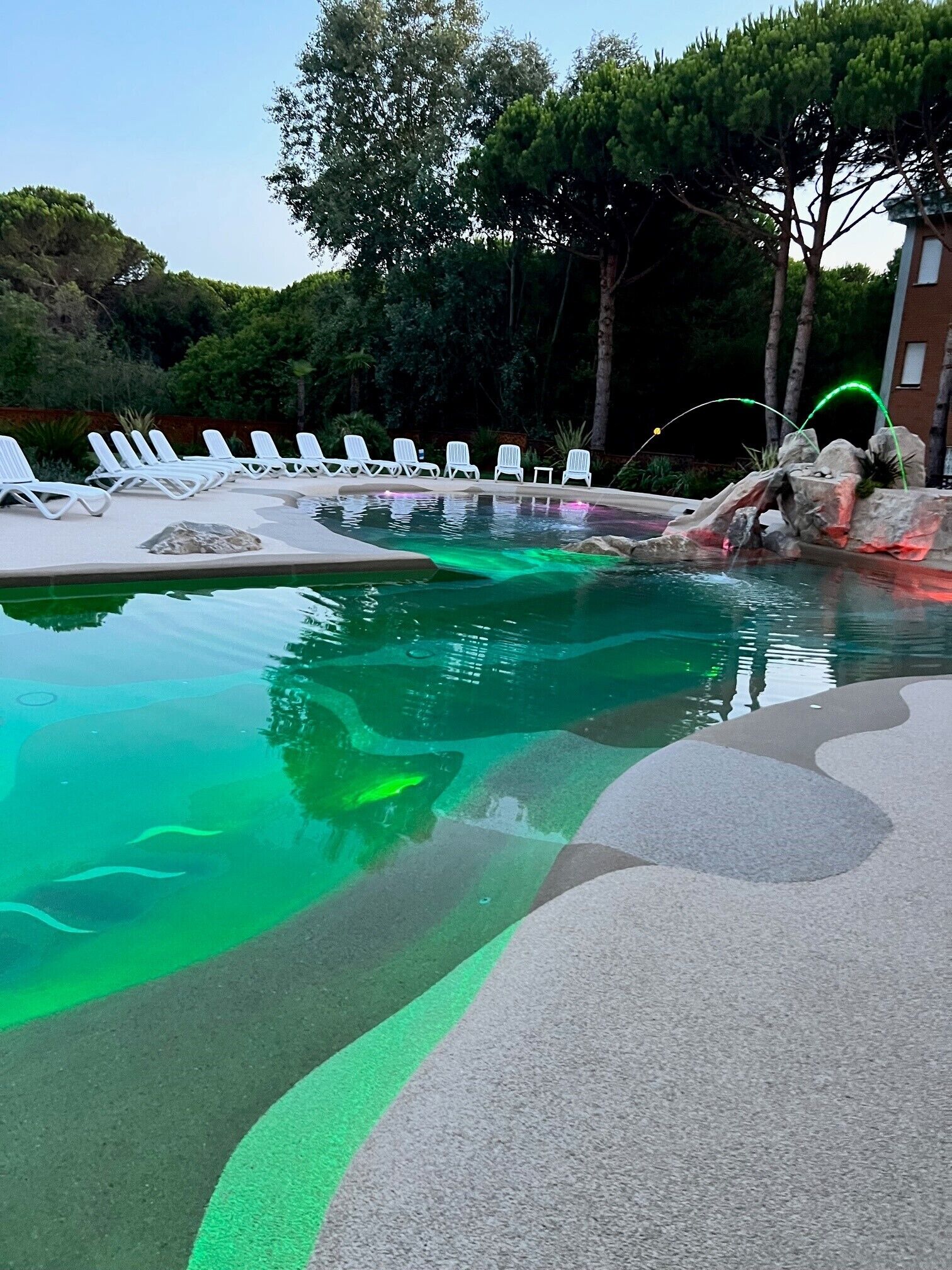 Una piscina con un diseño único, rodeada de sillones de descanso y un paisaje natural.
