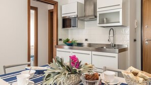 Une cuisine moderne avec des meubles blancs, des appareils en acier inoxydable et une table à rayures bleues, agrémentée de tasses et de bols blancs.