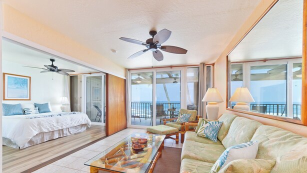 A spacious living area with a large glass coffee table, a sofa, and a ceiling fan. - Oceanfront Bliss: Pool, Hot Tub and Private Lanai (Kailua-Kona)