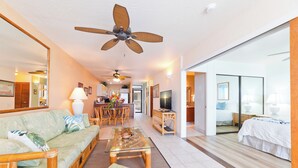 A spacious living area with a sofa, coffee table, and a dining set. A ceiling fan and a television are visible in the background. - Oceanfront Bliss: Pool, Hot Tub and Private Lanai (Kailua-Kona)