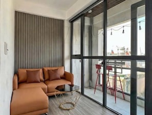 A modern living area with a sofa, a small table, and a view through large glass doors to an outdoor balcony. - Charming 1-bedroom apartment in Saigon Ward, Hochiminh city (Hồ Chí Minh)