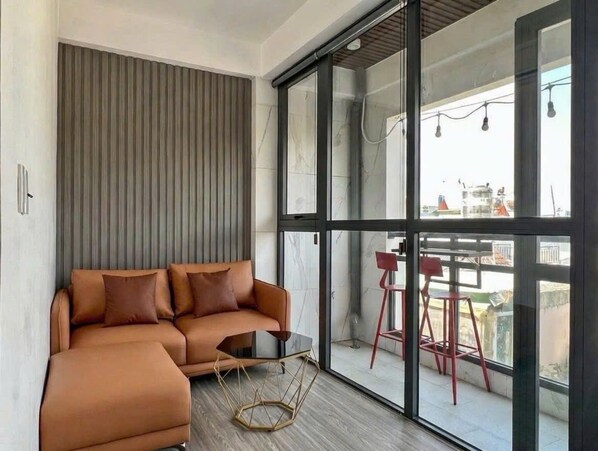 Ein zeitgemäßer Wohnbereich mit einer Couch, einem kleinen Tisch und Blick durch große Glasfenstertüren auf einen Außenbalkon.