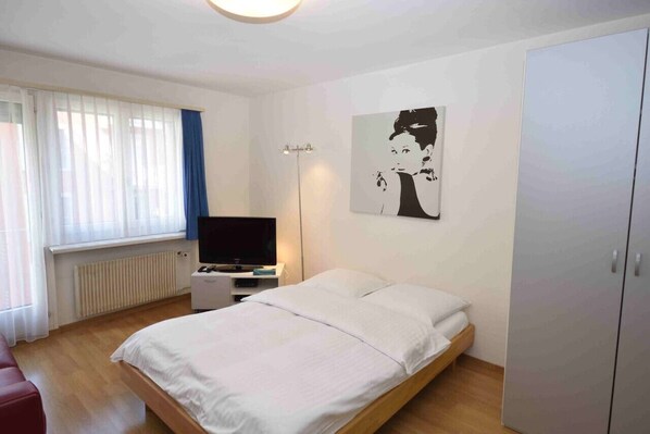 A bedroom with a bed, a TV, a wardrobe, and a painting on the wall. - Modern studio near main station (Crown 16) (Zürich)