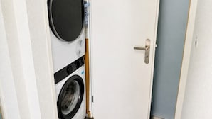 A laundry room with a washing machine and dryer, a door with a handle, and a blue wall. - Studio in a perfect location (Stork 35) (Zürich)