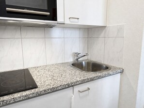 A kitchen with white cabinetry, a granite countertop, a stainless steel sink, and a built-in microwave. - Studio in a perfect location (Stork 35) (Zürich)
