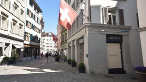 A street with buildings, a flag, and a storefront with a sign. - Studio in a perfect location (Stork 35) (Zürich)