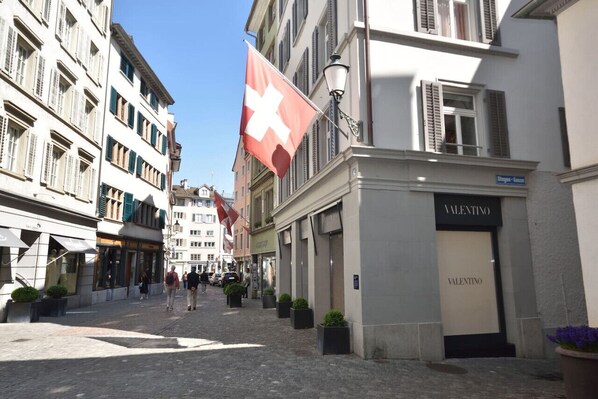 Rua com edifícios, uma bandeira e uma loja com uma placa.