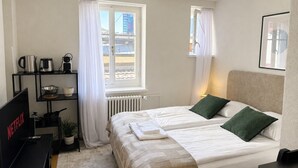 A hotel room with a bed, a desk with a computer, a radiator, and a window with curtains. - Studio in a perfect location (Stork 35) (Zürich)