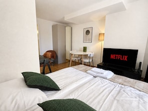 Quarto de hotel com cama, escrivaninha, cadeira, televisão e luminária.
