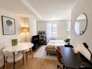 Quarto de hotel moderno com cama, escrivaninha, televisão e área de refeições.
