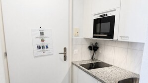 A small kitchen with white cabinets, a stainless steel sink, a black microwave, and a paper with QR code on the door. - Studio in a perfect location (Stork 35) (Zürich)